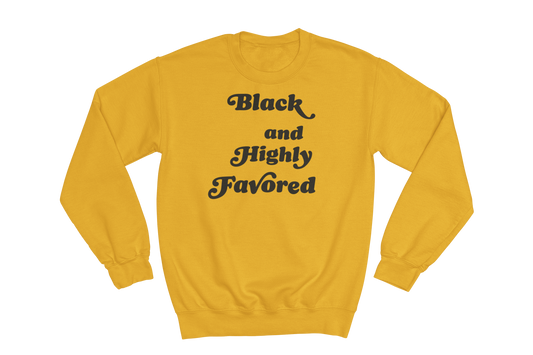 Gold crewneck sweatshirt featuring the phrase 'Black and Highly Favored' printed in stylized black script font on the chest.